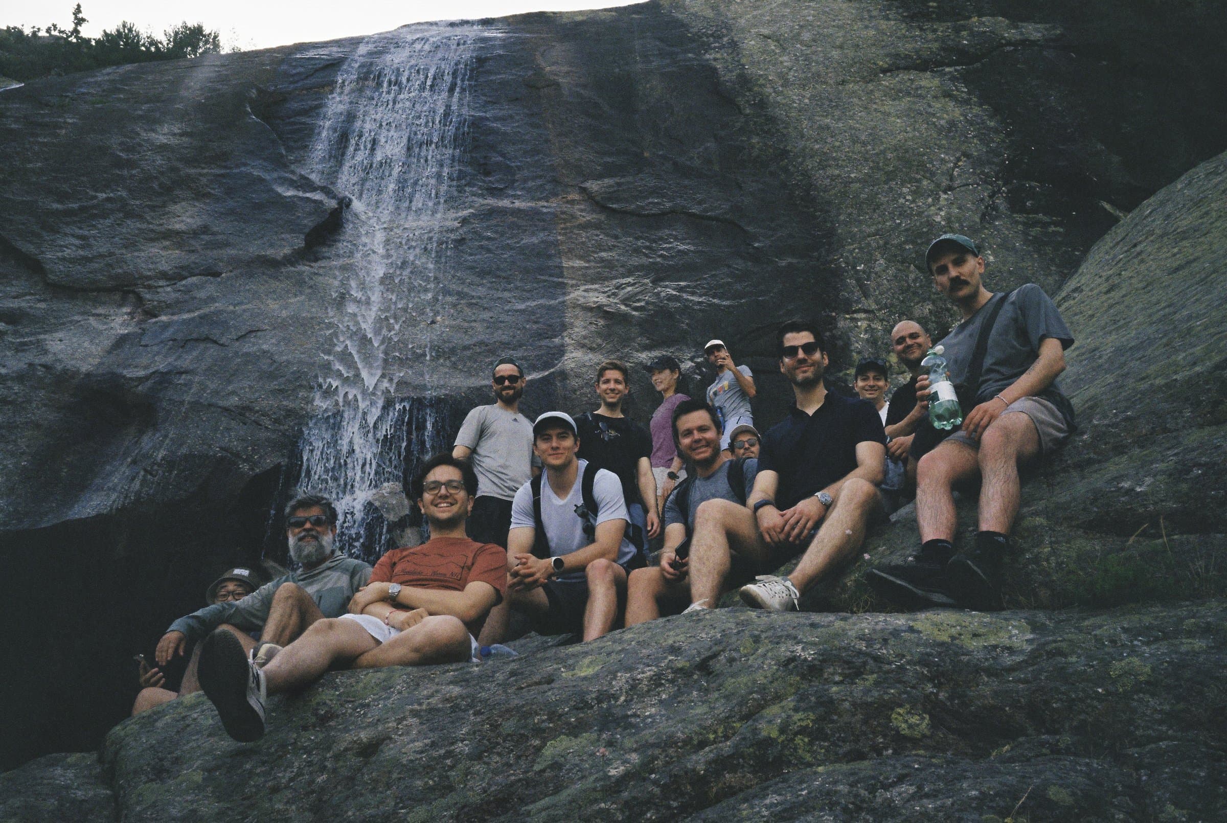 The Causa Prima team sitting on rocks below a waterfall during the 2026 offsite